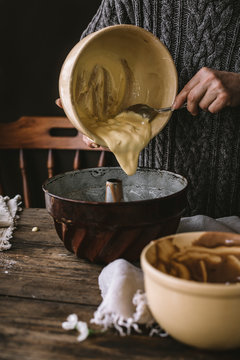 A woman cooking a bundt cake at home in a rustic kitchen, on a wooden table.