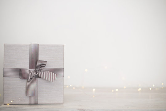 Light Christmas background, banner with New Year's decor: a big beautiful white wrapped gift with a bow on a white wooden table. Free space for text.