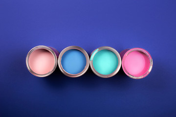 Four open cans of paint on blue background. Coral, blue, pink, turquoise colors. Top view.