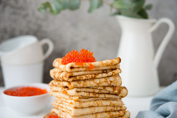 Close up classic thin lace pancakes on a wooden plate with red caviar on a light background. A traditional dish for Shrove Tuesday