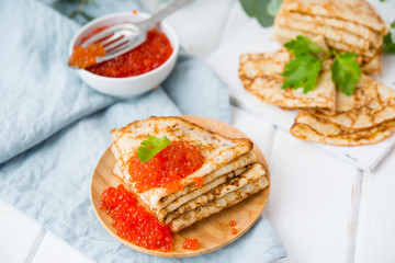 Classic thin lace pancakes on a wooden plate with red caviar on a light background. A traditional dish for Shrove Tuesday