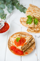 Classic thin lace pancakes on a wooden plate with red caviar on a light background. A traditional dish for Shrove Tuesday