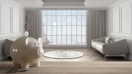Wooden table top or shelf with white piggy bank with coins, modern panoramic living room, sofa, carpet, expensive home interior design, renovation restructuring concept architecture
