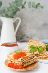 Classic thin lace pancakes on a wooden plate with red caviar on a light background. A traditional dish for Shrove Tuesday