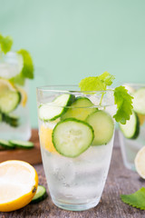 Refreshing detox water with cucumber, lemon and fresh mint on a light green background. Organic, vegan beverage.