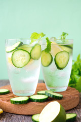 Refreshing detox water with cucumber, lemon and fresh mint on a light green background. Organic, vegan beverage.