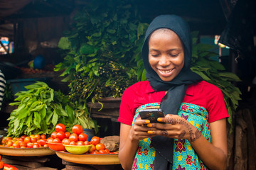 young african woman selling in a local market smiling while using her mobile phone