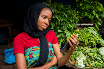 young african woman selling in a local market feeling sad and dejected while looking at her phone