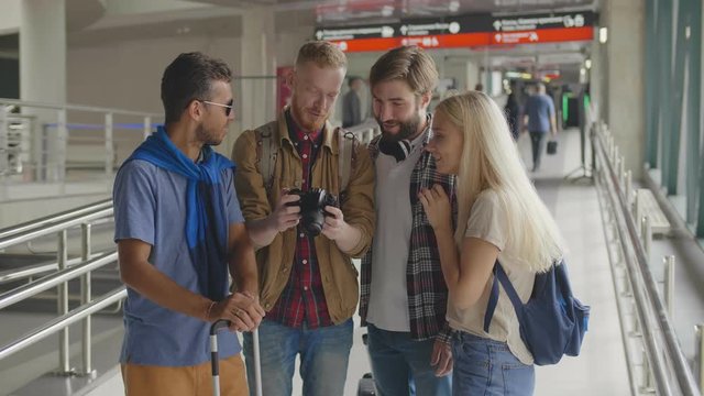 Four travelers watching holidays pictures on camera standing at railway station