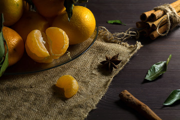 fresh orange tangerines with green leaves on wooden background. ripe fruits on dark table with sticks of cinnamon and spices. low key.