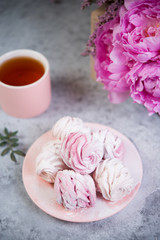 Homemade berry marshmallow in a plate is on the table with a Cup of tea. Powdered sugar falls on top of marshmallows..