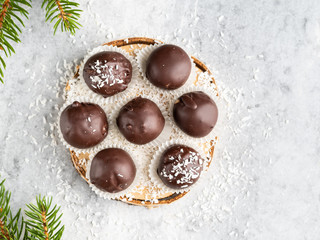 Winter dessert, healthy sugarfree peanut butter truffles covered by dark chocolate and coconut shred, christmas and new year background, fir tree branches, wooden plate, white background