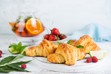 Still life of fresh morning croissants and berry tea in a glass teapot on a white wooden background. Horizontal photo of Breakfast.