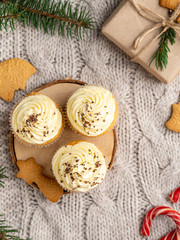 Christmas and winter dessert, gingerbread cupcakes with cream cheese frosting and chocolate. Frame of cinnamon, present gift box covered in paper, spruce branches, candy canes. Flat layout, still life