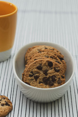 Homemade chocolate cookies in a porcelain plate and a yellow cup of coffee. Closeup. Out of focus background.