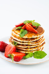American pancakes lined with strawberries and honey poured on a white background. Classic American Breakfast.