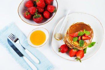 American pancakes lined with strawberries and honey poured on a white background. Classic American Breakfast. Top view