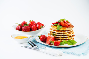 American pancakes lined with strawberries and honey poured on a white background. Classic American Breakfast.