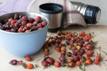 Dried rose hips in a bowl and scattered on a wooden table