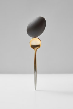 Golden spoon with black egg is standing on a white table on a gray background.