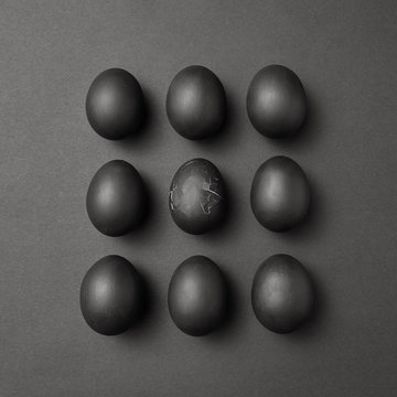 Easter pattern of black eggs on a black background. One broken egg in the middle.