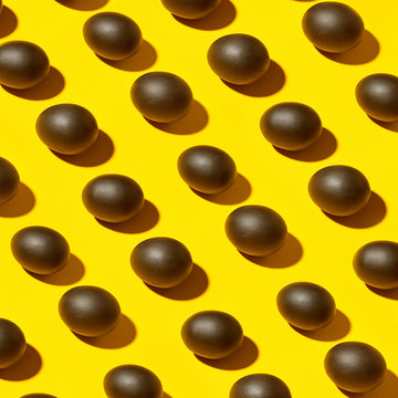 Easter pattern from black eggs with shadows on a yellow background,