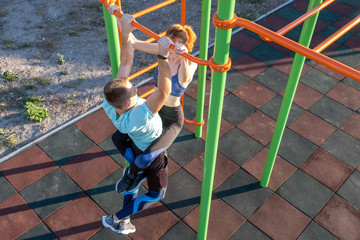 Young fit athlete working out at outdoor gym making dipping pull ups exercise using dip rings with...