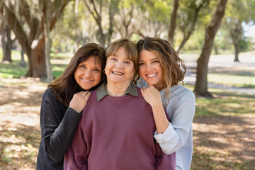 Three generations of related women smiling and embracing one another while standing outside.