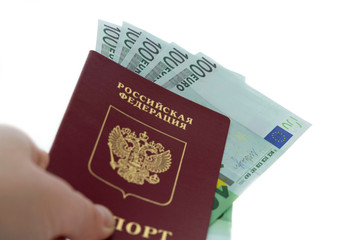 Fototapeta premium Close-up of a Russian foreign passport with euro banknotes inside in a male hand in defocus on a white background