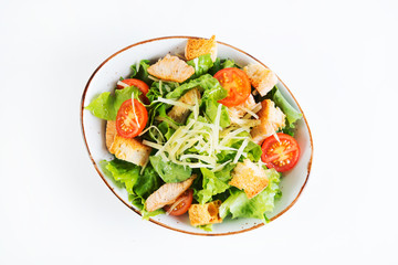 Caesar salad with chicken breast, tomatoes and wheat croutons in a plate on a white background. Horizontal photo. Top view