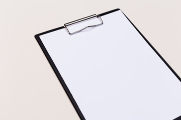Clipboard with a white sheet and pen on a light background. View from above. space for text