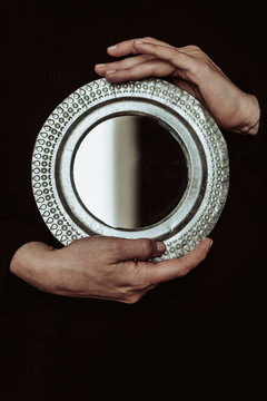 Anonymous hands holding a round mirror