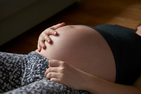 Young pensive pregnant lady sitting on floor in room