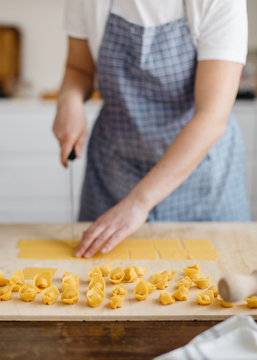 Lines of raw freshly home made cappelletti stuffed pasta with unrecognizable woman cutting fresh dough pasta on the background