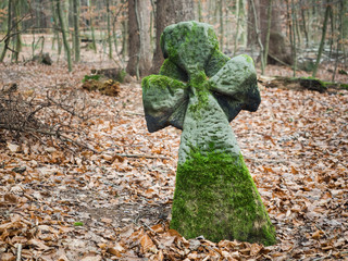 Ein altes mit Moos besetztes Kreuz aus Stein steht im Wald.
