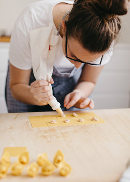 Woman bending on kitchen table while stuffing pasta dough in order to make typical pasta called cappelletti
