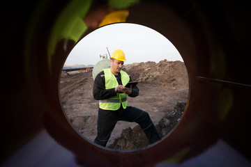 Shot of an oilfield worker checking quality of gas pipes at construction site.