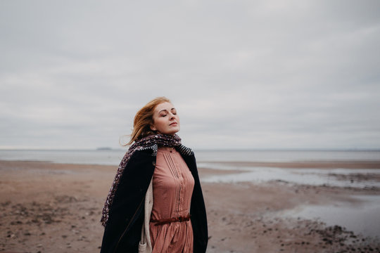 Thoughtful romantic woman on the shore of the bay on a cloudy windy day.
