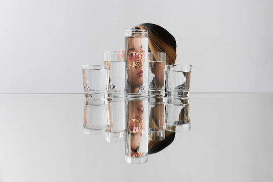 Contorted woman in sunglasses behind glasses with water