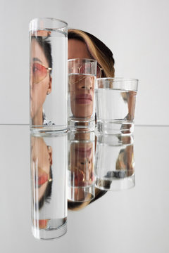 Woman wearing sunglasses distorted through glasses with water