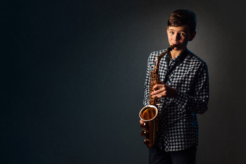 A boy on a dark background with a searchlight plays saxophone
