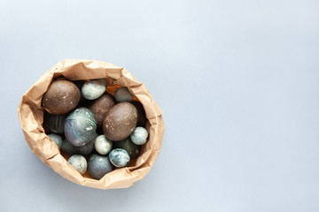 Creatively painted chicken and quail Easter eggs with natural hibiscus dye, look like sea stones in craft bag on a gray background. Happy Easter DIY concept. Soft slective focus. Flat lay, copy space