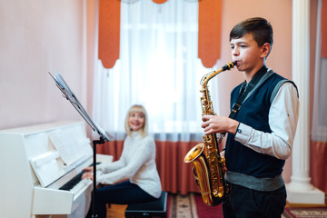 A teenage boy learns to play the saxophone in a music lesson to the accompaniment of a female...