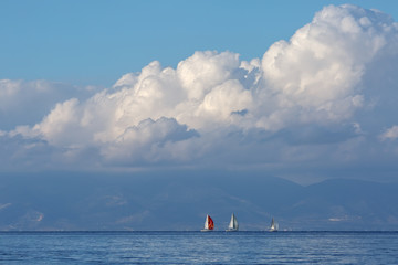 three sailboats in a blue sea against a background of mountains and white Cumulus clouds
