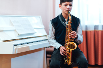 Fototapeta premium student boy plays saxophone while sitting at a music lesson in class
