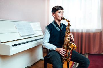 student boy plays saxophone while sitting at a music lesson in class