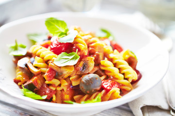 Fusilli pasta with cherry tomatoes, olives and champignon mushrooms. Bright wooden background. Close up. 