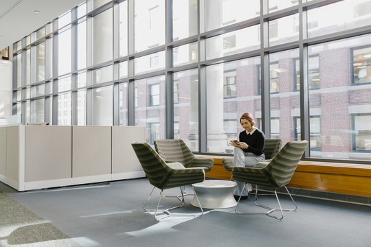 Hispanic Businesswoman Using Mobile Phone Alone In Office Lobby