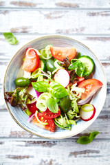 Healthy Salad with Cherry Tomatoes, Green Olives, Radish, Leek, Lettuce and Fresh Basil. Easy summer snack. Bright wooden background. Top view. 