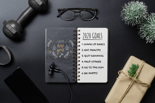 New Year Healthy Goals And Resolutions Concept. 2020 New Year's Goals Written On  Notebook Paper, And Dumbbells On Black Background, Fitness, Sport And Health Concept, Top View